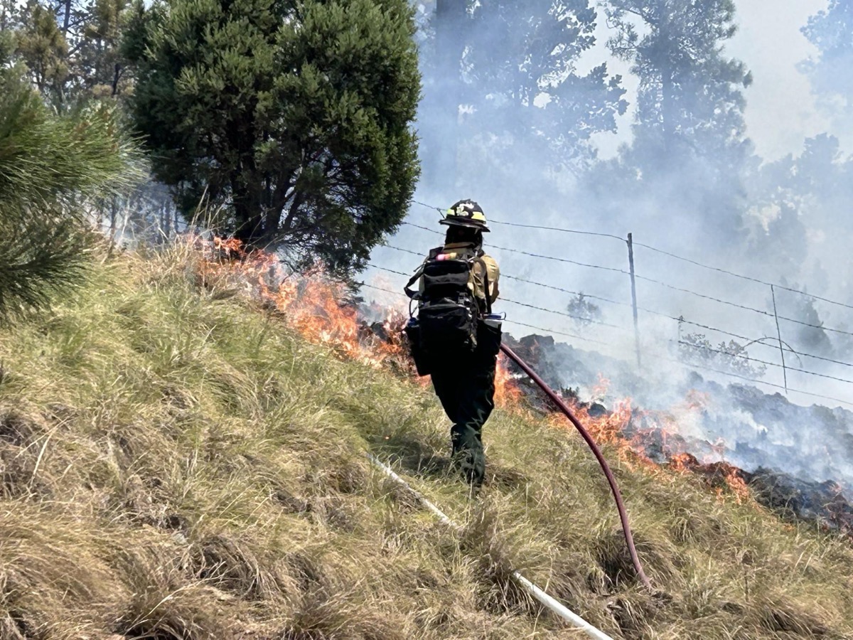 A wildland firefighter working a hose line on a burning hillside during the South Fork Fire